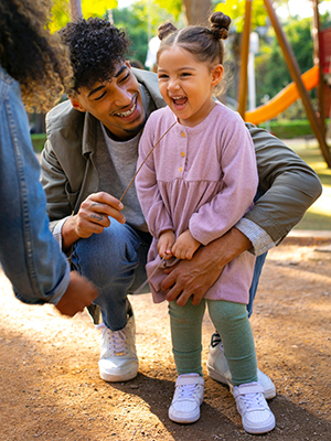 Father and daughter laughing together at a playground during a daycare visit.